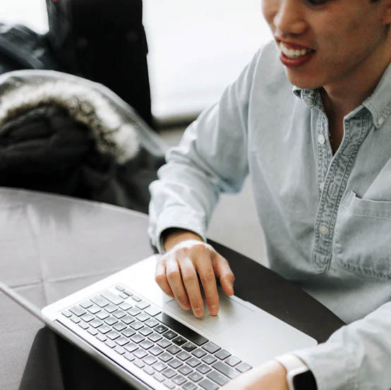 Student smiling whilst typing on a laptop on a glass table